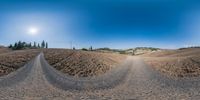 a large wide angle lens of dirt road with mountain in distance, at sunset in the distance is bright blue sky