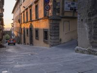 a car driving down an empty street in italy at sunset with buildings and signs above the street