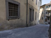 a narrow alley has buildings lining the street with windows and doors, including a small bench