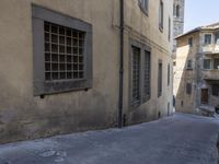 a narrow alley has buildings lining the street with windows and doors, including a small bench