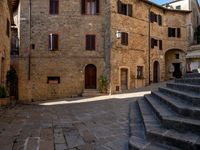 the stairs of a narrow cobblestone street lead up to an ancient building with multiple rooms