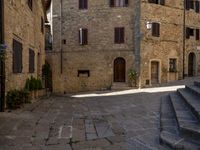 the stairs of a narrow cobblestone street lead up to an ancient building with multiple rooms