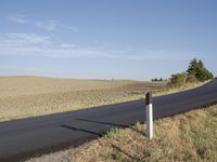 a street sign is near an empty road in the countryside area that stretches into a barren field