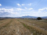 an empty rural area with hills and electrical wires in the distance under blue skies with clouds in the sky