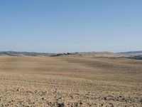 there is a lone red barn in the middle of a barren field of dirt and sparse grass