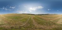 an empty open field in the middle of a blue sky with clouds in the background