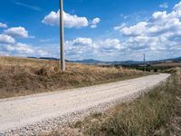 a lone road with rocks and some dirt and some clouds on top of it and a telephone pole in the middle