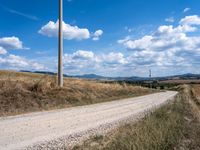 a lone road with rocks and some dirt and some clouds on top of it and a telephone pole in the middle