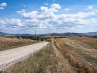 a lone road with rocks and some dirt and some clouds on top of it and a telephone pole in the middle