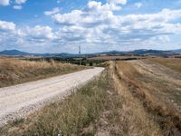 a lone road with rocks and some dirt and some clouds on top of it and a telephone pole in the middle