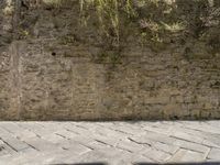 a person sits on a bench near a stone wall with moss growing on it, looking down the street