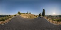 a curved road going around the corner near a hill with a lone tree on it