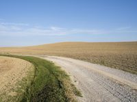 a gravel road running through the grass and field land near a large field and farm land