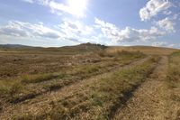 a dirt road through a grassy field near a lone hill, under a sky full of clouds