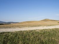 a person on a bike in front of a hill that is dirt and grass and there are two hills behind them