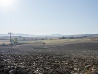 a field with lots of rocks, dirt and power lines near the mountaintop with the sun