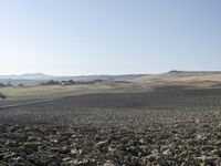 a field with lots of rocks, dirt and power lines near the mountaintop with the sun