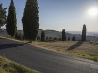 an open road with trees in front of it and the sun shining over the hills and valley