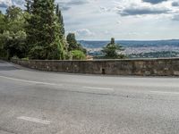 a curve in the road with trees and mountains in the background on a cloudy day