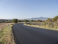 a rural road with no cars on the side of it near a grassy and mountains