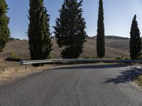 the road is paved with an empty curve next to trees in the hills and fields