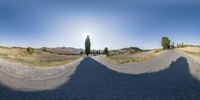 a panoramic image of a road with shadows from the pavement and the sun casting a shadow of trees in the distance