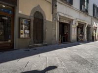 a shadow of a person walking on the sidewalk outside of a building in italy, on a sunny day