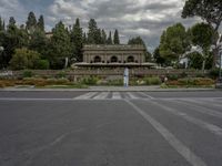 an empty street with no traffic in front of a building surrounded by trees and flowers