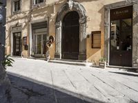 a cat sits on the sidewalk next to a large building with many doors and windows