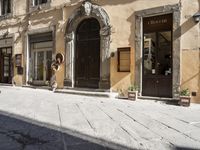 a cat sits on the sidewalk next to a large building with many doors and windows