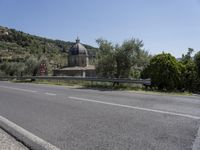 a view of a country road in the mountains with a church on it and a steep hill behind