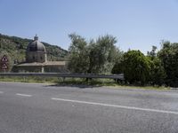 a view of a country road in the mountains with a church on it and a steep hill behind