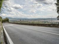 a paved road under cloudy skies on a nice day, with mountains and greenery in the background