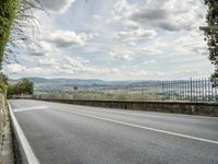 a paved road under cloudy skies on a nice day, with mountains and greenery in the background