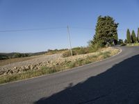 a bike rider riding down a road beside a hill and tree line next to a hill