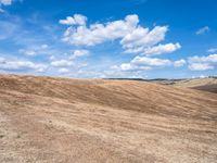 a vast open hill, covered in yellow grass and straw, under clouds, against a blue sky