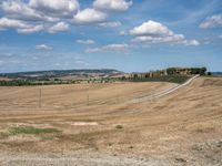 field with small road passing by the rural countryside and rolling hills in the background under clouds