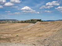 field with small road passing by the rural countryside and rolling hills in the background under clouds