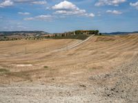 field with small road passing by the rural countryside and rolling hills in the background under clouds