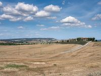 field with small road passing by the rural countryside and rolling hills in the background under clouds