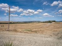 field with small road passing by the rural countryside and rolling hills in the background under clouds