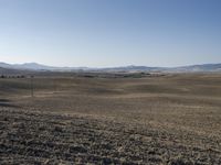 the hills are empty and visible in this landscape of sparse farmland, and a dirt road leading