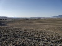 the hills are empty and visible in this landscape of sparse farmland, and a dirt road leading