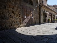 a shadow is cast on the ground in the foreground, there is an old building next to some brick walls