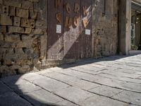 a shadow is cast on the ground in the foreground, there is an old building next to some brick walls