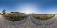 a fish - eye photo of a rural road with mountains in the background and grass on the side of it