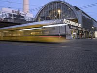 a train traveling past an art nouveau building in front of a train station at twilight