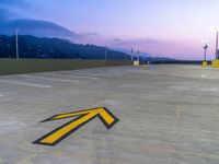 an arrow painted on the concrete parking lot at twilight near mountains and city buildings at dusk