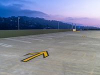 an arrow painted on the concrete parking lot at twilight near mountains and city buildings at dusk