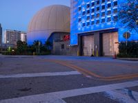 a clock is seen at the top of the building at twilight in front of a building with a large sphere shaped space - like structure on top